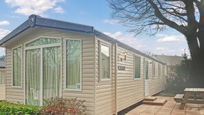 A mobile home with large windows, a patio area, and a number '12' sign. - Sunnyvale Willow 3 Pet Friendly (Saundersfoot)
