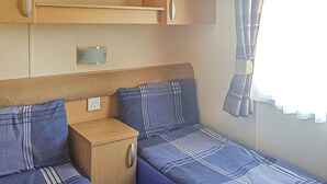 A compact RV interior with a bed, a small cabinet, and a power outlet. - Sunnyvale Willow 3 Pet Friendly (Saundersfoot)