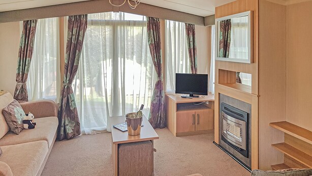 A living room with a sofa, a TV, a fireplace, and a table with a bottle. - Sunnyvale Willow 3 Pet Friendly (Saundersfoot)