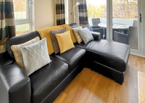 Ein schwarzes Ledersofa mit mehreren Kissen, ein Holzboden und Blick auf Gartenmöbel durch eine Glastür.
