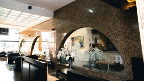 A lobby with a reception desk, seating area, and a large arched mirror reflecting the interior. - Lucape Palace Hotel (Barbacena)