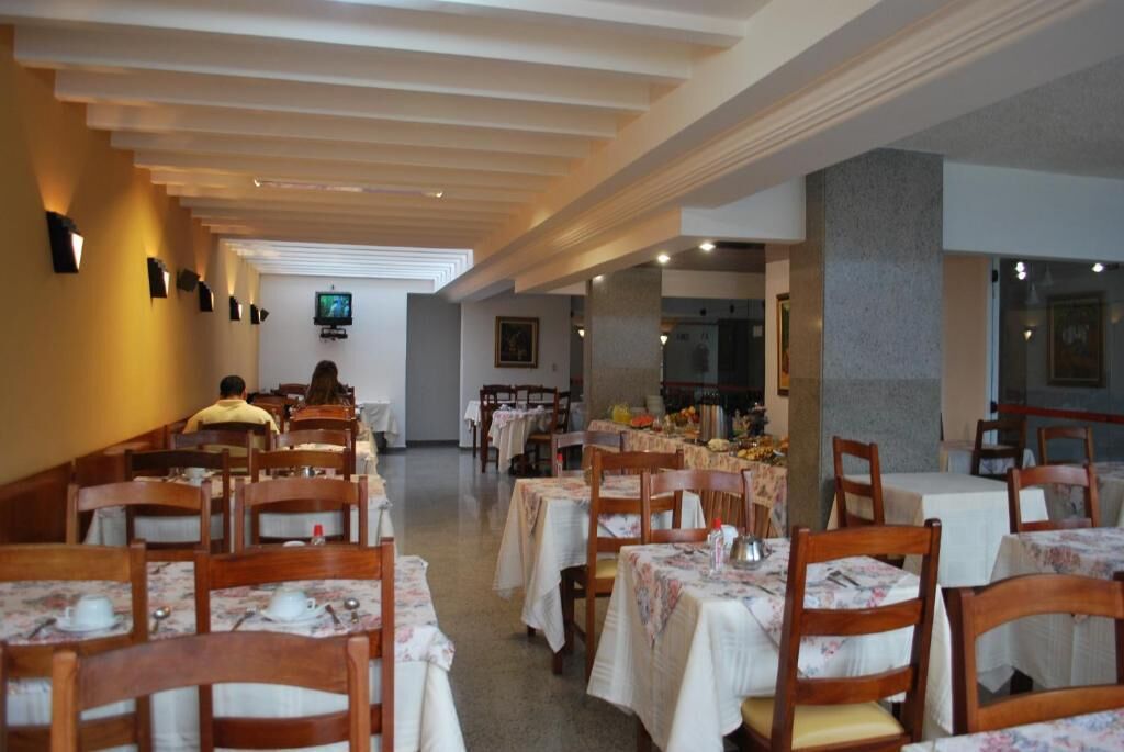 A restaurant with wooden chairs and tables, a television on the wall, and a person sitting at a table.