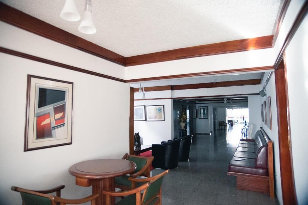 A hotel lobby with a round wooden table, green chairs, a bench, and framed artwork on the walls.