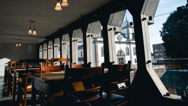 A dining area with wooden tables and chairs, large windows with a view of a historic building. - Lucape Palace Hotel (Barbacena)