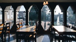 An interior with tables and chairs, large arched windows, and hanging pendant lights. - Lucape Palace Hotel (Barbacena)