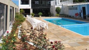 A modern building with a reflective glass facade, a swimming pool, and outdoor seating. - Lucape Palace Hotel (Barbacena)