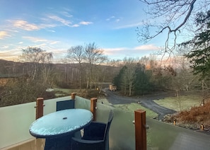 A balcony with a table and chairs, overlooking a rural landscape with trees and a road. - 2 bedroom accommodation in Water Yeat, Nr Coniston (Water Yeat, Nr Coniston)