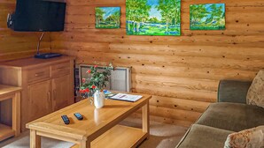 En stuga med träpanel på insidan, inredd med en soffa, ett soffbord med en vas med blommor, en tv och tavlor på väggen.