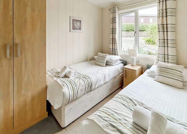 Un dormitorio con dos camas, un armario de madera, una mesita de noche, una ventana con cortinas y un cuadro colgado en la pared.