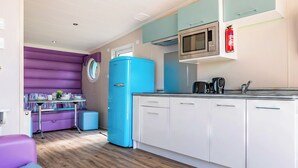 Eine kleine Küche mit blauem Kühlschrank, weißen Schränken, einer Mikrowelle und einer Kaffeemaschine.