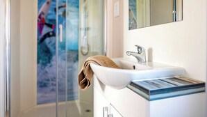Ein modernes Badezimmer mit Duschkabine aus Glas, einem weißen Waschbecken und einem Handtuch an der Wand.
