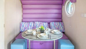 Ein Zimmer mit einem violetten Sofa, einem runden Tisch gedeckt mit Tellern, Gläsern und einer kleinen Pflanze.