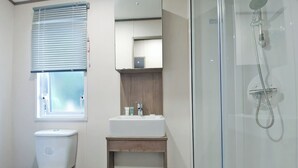 A bathroom with a toilet, sink, mirror, and shower.