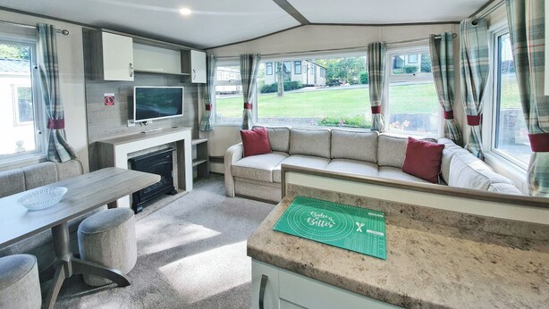 A compact RV interior with a kitchenette, seating area, and large windows.