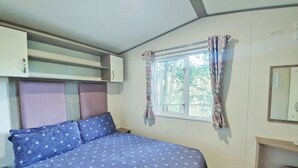 A bedroom with a bed, a nightstand, a dresser, a window with curtains, and a mirror.