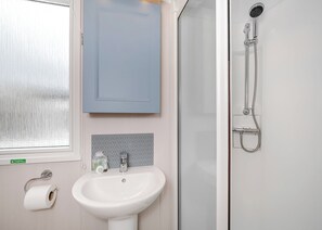 A bathroom with a white sink, a mirror, a shower, and a window with frosted glass.