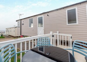 A mobile home with a deck, outdoor seating, and a window with a view.