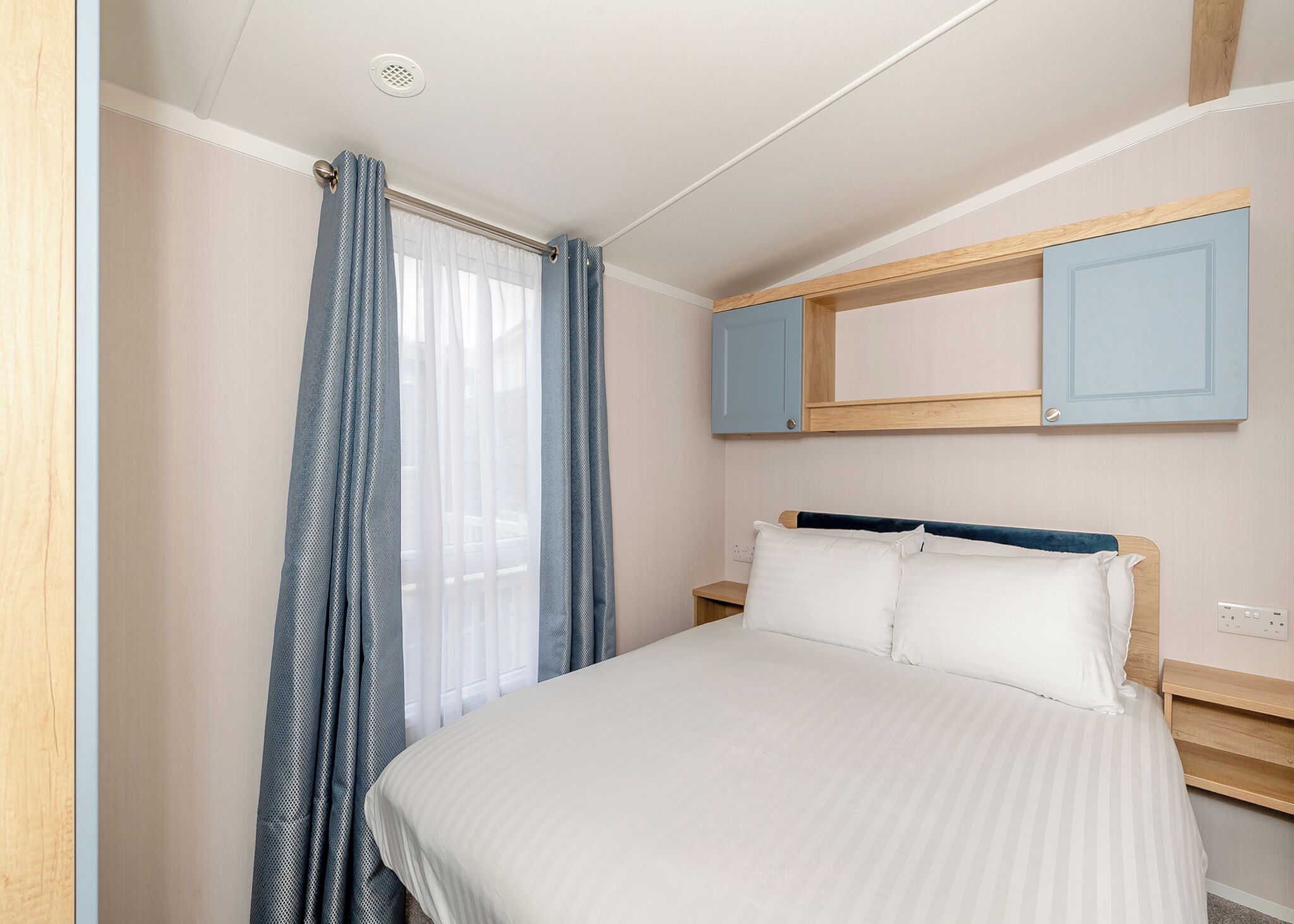 Un dormitorio con cama, mesita de noche, espejo y ventana con cortinas.