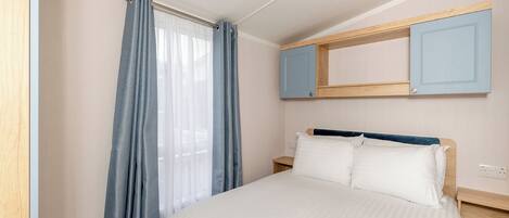 Un dormitorio con cama, mesita de noche, espejo y ventana con cortinas.
