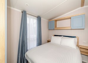 A bedroom with a bed, a nightstand, a mirror, and a window with curtains.