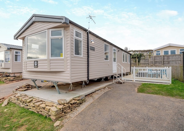A mobile home with a front porch, a small deck, and a fenced backyard.