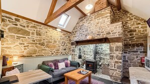 Una habitación acogedora con pared de piedra, chimenea, sofá, mesa y ventana.