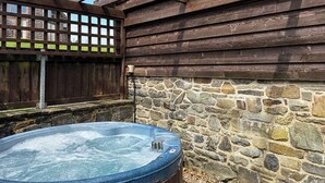 Un jacuzzi junto a un muro de piedra y una valla de madera.