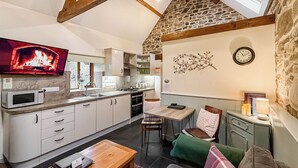 Una cocina acogedora con pared de piedra, vigas de madera, un televisor de pantalla plana y una zona de comedor con mesa y sillas.