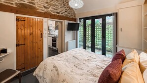 Un dormitorio con pared de piedra, puerta de madera, cama con ropa de cama estampada, televisor y vistas por una puerta corredera.