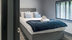 A modern bedroom with a large bed, grey walls, and a window with blinds.
