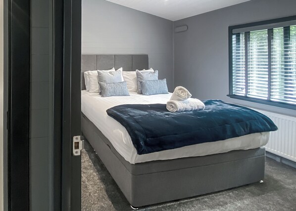 A modern bedroom with a large bed, grey walls, and a window with blinds.