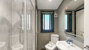 A bathroom with a glass-enclosed shower, a toilet, a sink, and a window with blinds.