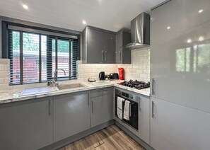 A modern kitchen with grey cabinets, a stainless steel range hood, a gas stove, a sink, and a window with blinds. - Traditional pine lodge with a modern twist. (Snowdonia)