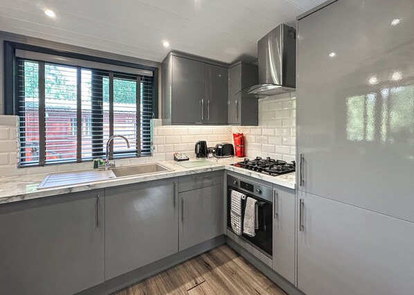 A modern kitchen with grey cabinets, a stainless steel range hood, a gas stove, a sink, and a window with blinds.