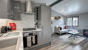 A modern kitchen with a built-in oven and gas stove, a grey sofa, and a fireplace.
