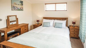 A bedroom with a wooden bed, two bedside tables, a desk with a chair, a mirror, and a window with blinds. - Contemporary lodge furnished to a very high standard. (Tunstall, Nr Hull)