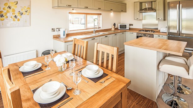 A modern kitchen with white cabinets, a dining table set for four, and a bar area with stools. - Contemporary lodge furnished to a very high standard. (Tunstall, Nr Hull)