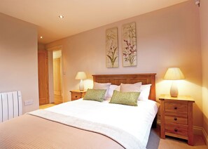 A bedroom with a bed, two bedside tables with lamps, a radiator, and two wall-mounted floral paintings. - A stunning luxury lodge, perfect for a couples retreat or family break. (West Tanfield)