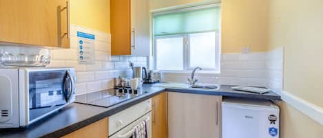 Una cocina compacta equipada con microondas, tostadora, hervidor, lavabo y refrigerador pequeño.