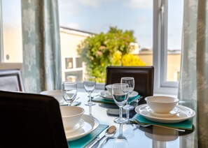 A dining table set with plates, bowls, wine glasses, and cutlery, with a view of greenery and buildings through the window.