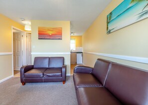 A hallway with two leather sofas, a painting of a sunset, and a kitchen area.