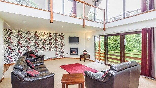 A spacious living room with a high ceiling, a fireplace, a TV, and a large sliding glass door leading to a garden.