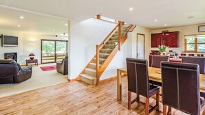 A spacious living area with a wooden staircase, a dining table with chairs, a kitchen area, and a fireplace.