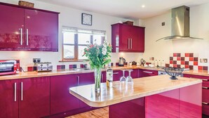 A modern kitchen with red cabinets, a wooden countertop, a central island with a vase, and a stainless steel range hood.