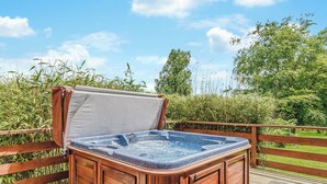 A hot tub on a wooden deck with a wooden railing, surrounded by greenery.