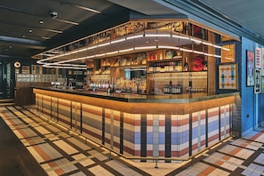 Zona de bar con suelo de baldosas, mostrador de madera y diversas botellas y vasos.