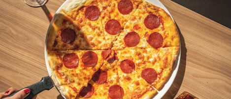 Una pizza de pepperoni sobre un plato blanco, con un cortador de pizza y una botella, todo sobre una mesa de madera.