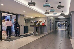A hotel lobby with a reception desk, a man in uniform, and a glass elevator. - City Sleeper at Royal National Hotel (London)