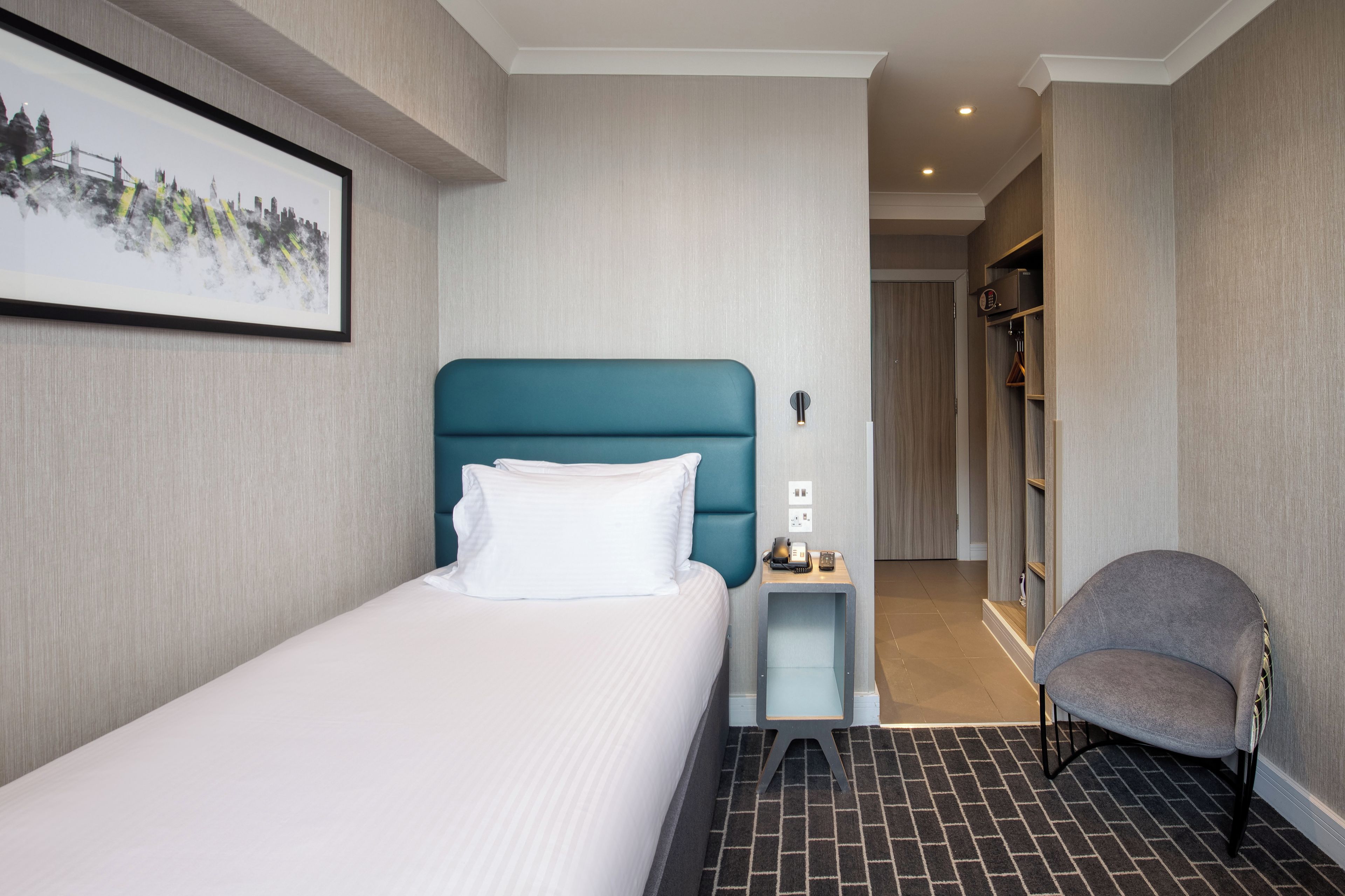 A hotel room with a bed, a chair, a nightstand, a telephone, and a picture on the wall.