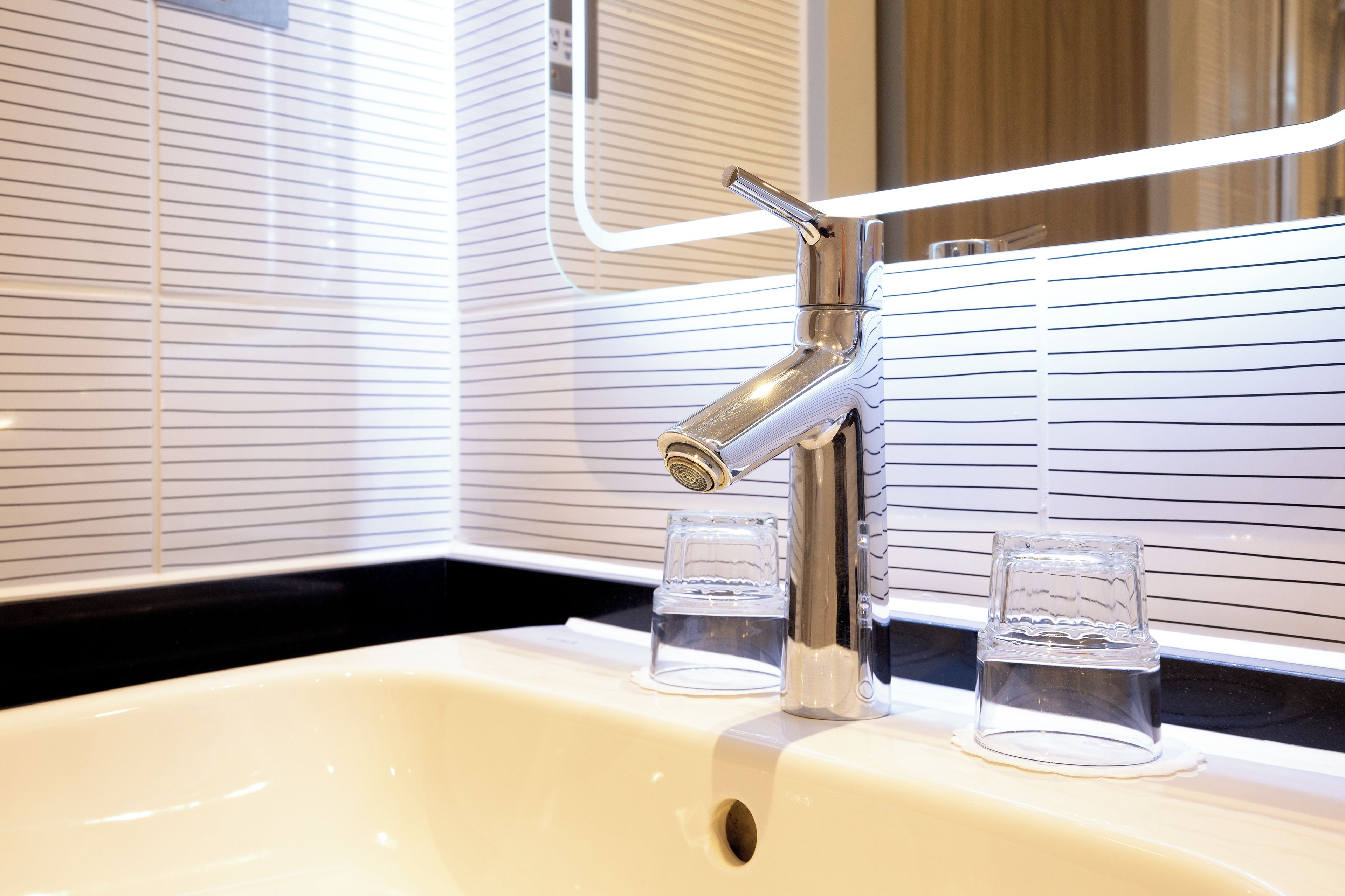 Un baño con lavamanos blanco, grifo cromado y dos vasos de vidrio sobre la encimera.